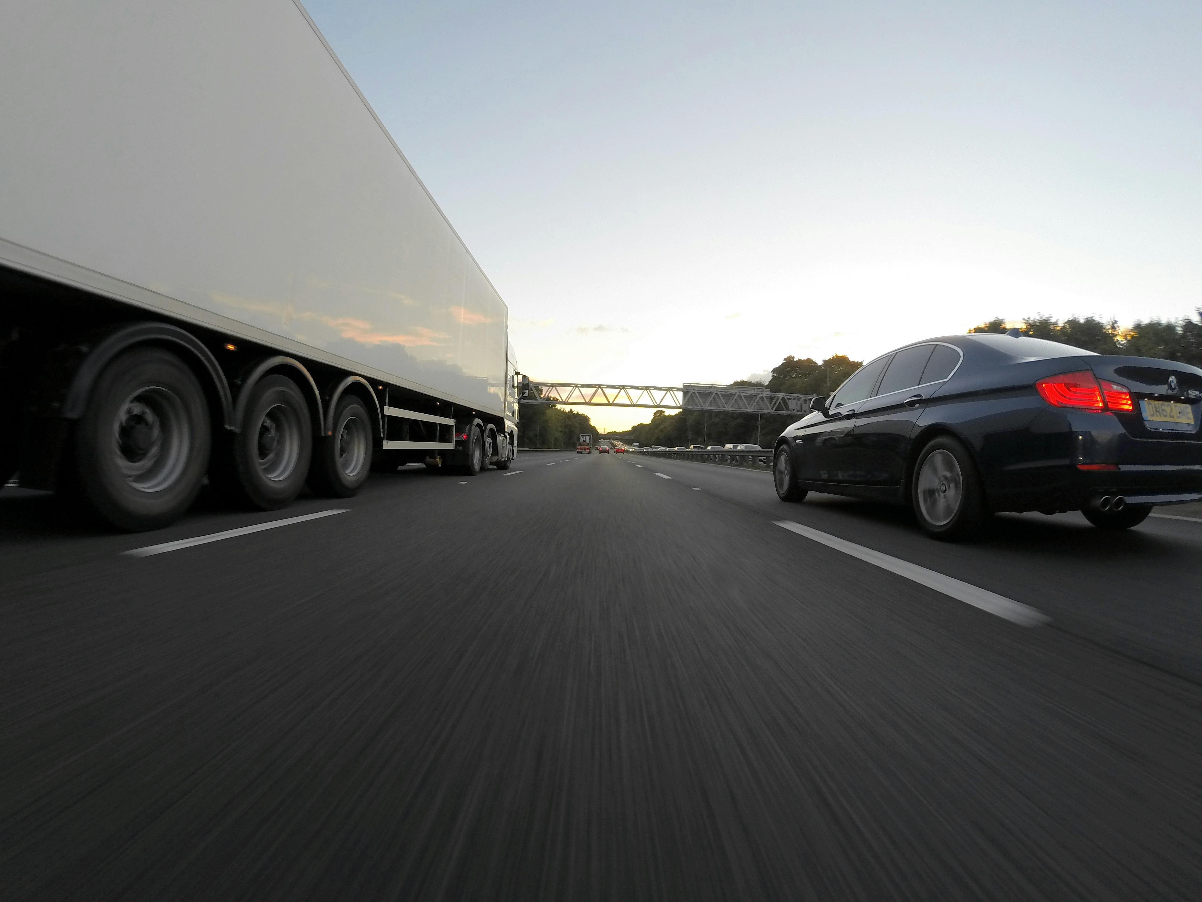 Lorry and car driving on a motorway at sunset, illustrating AM2PM Tyres's 24/7 roadside Lorry Tyres service in Reading.
