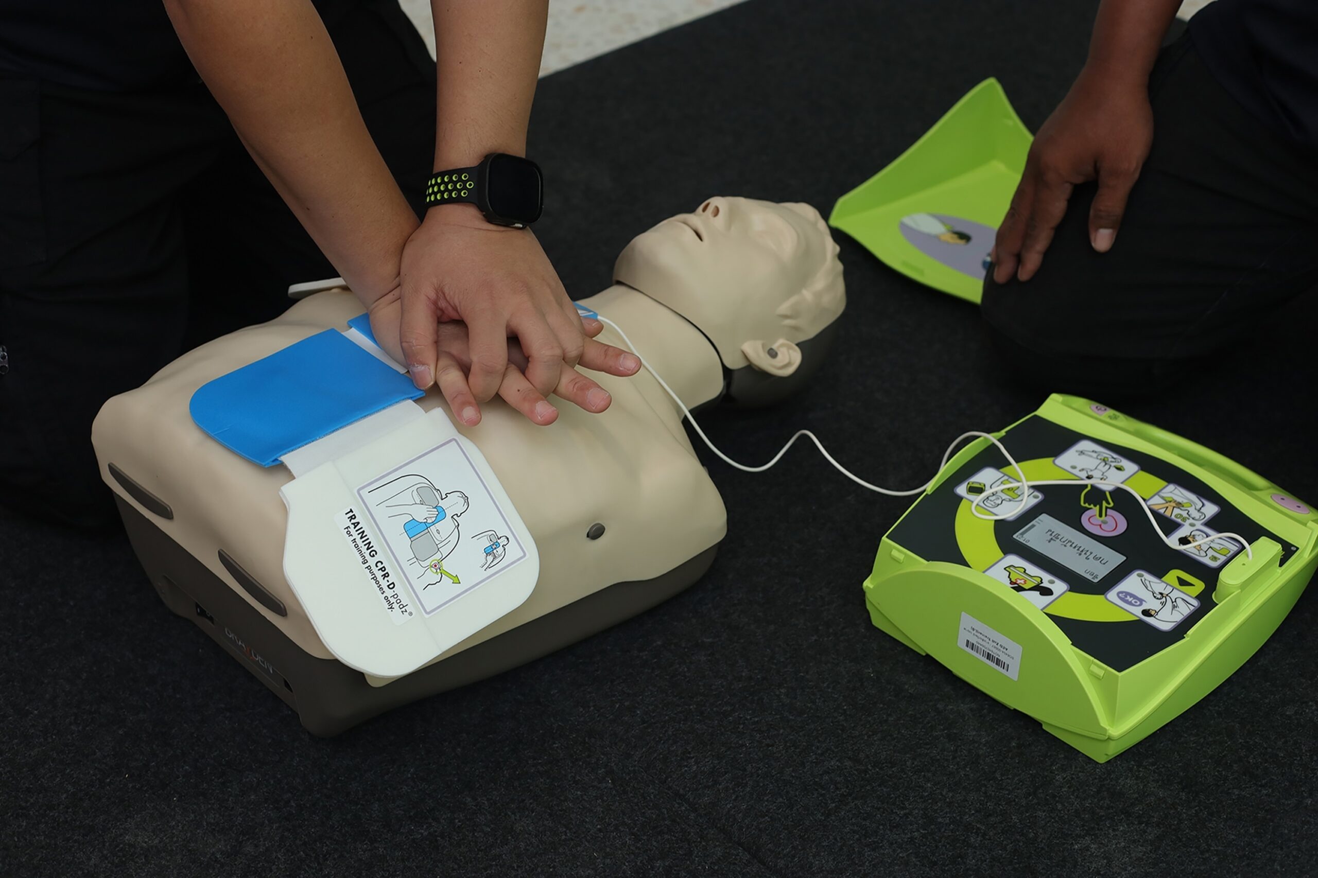 Person performing CPR on a training mannequin with an AED nearby, illustrating {{company_name}}'s {{search_term}} in {{place}}.