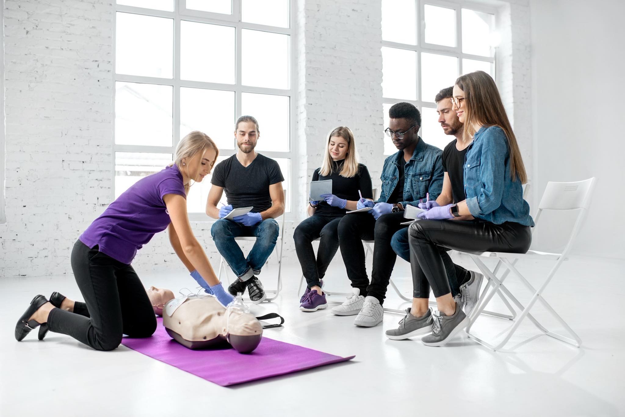 A group of people in a bright room learning CPR techniques on a mannequin, part of a {{search_term}} by {{company_name}}.