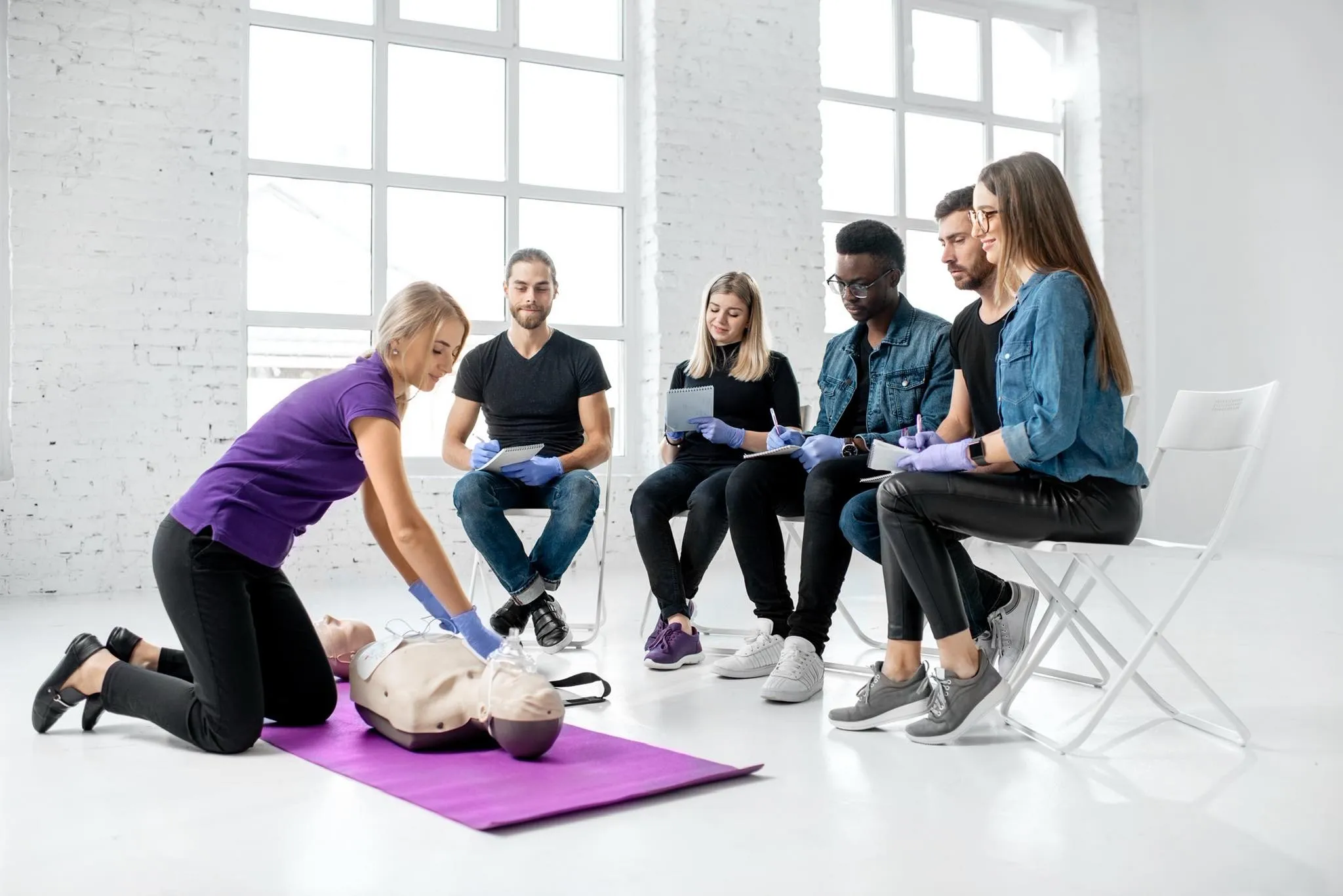 A group of people in a bright room learning CPR techniques on a mannequin, part of a Health &amp; Safety Training Course by AFW Training Ltd.