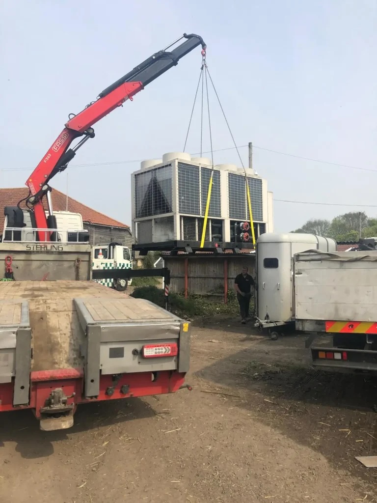 A crane lifts a large industrial chiller unit onto a flatbed truck, illustrating London Metal &amp; Recycling Ltd's recycling services for ⁠Commercial Kitchen, Chiller &amp; Ac Unit Recycling in Willesden.