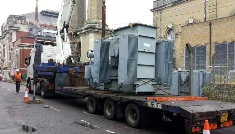 A large industrial transformer being loaded onto a flatbed truck, illustrating heavy equipment recycling by London Metal &amp; Recycling Ltd in Acton.
