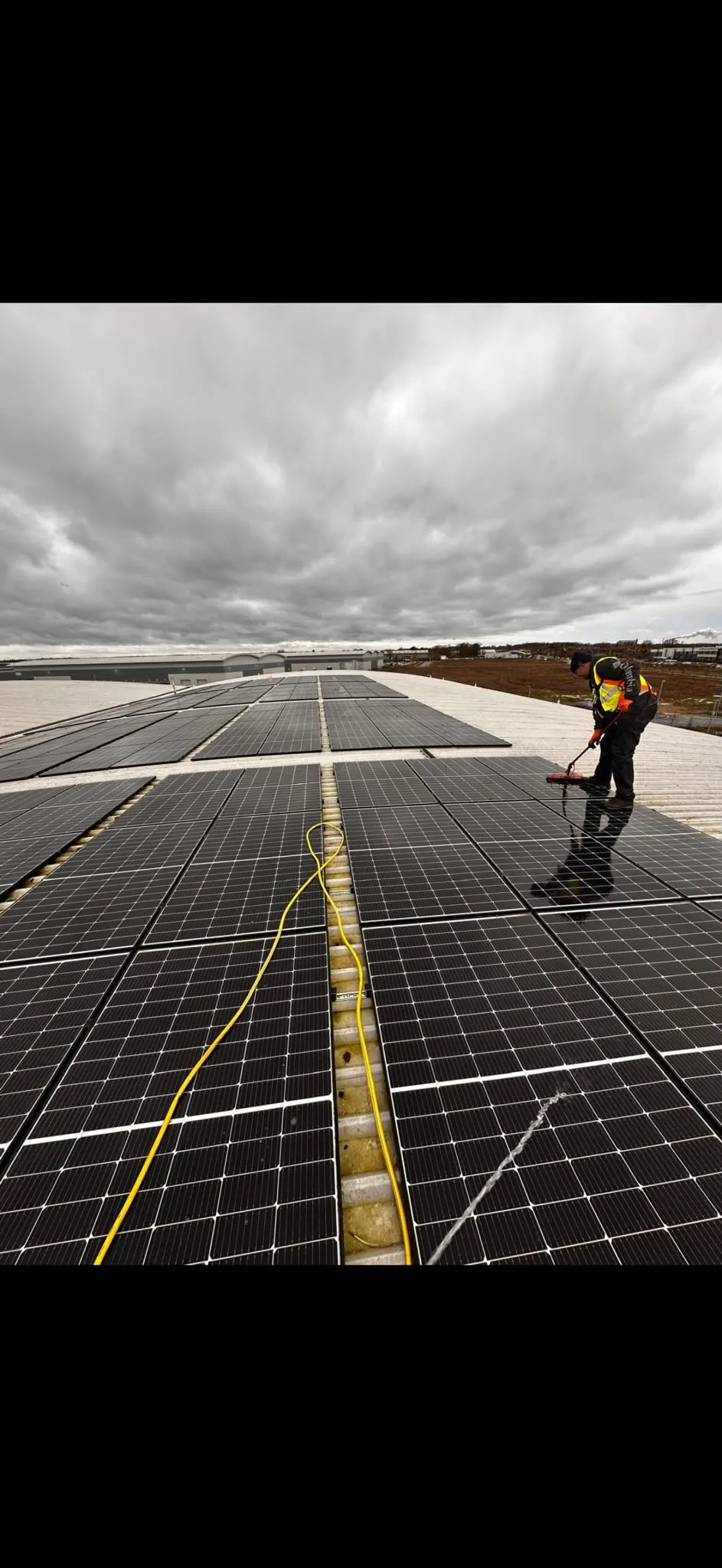 Electrician cleaning solar panels on a rooftop under cloudy skies, showcasing ICE Electrical Solutions's expertise in Solar Installation.