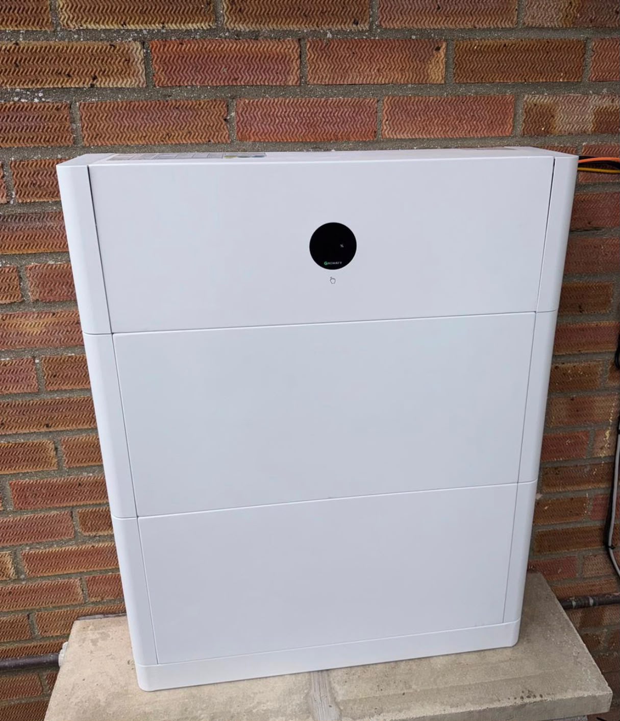 A modern battery storage unit installed against a brick wall, part of {{company_name}}'s solar solutions in {{place}}.