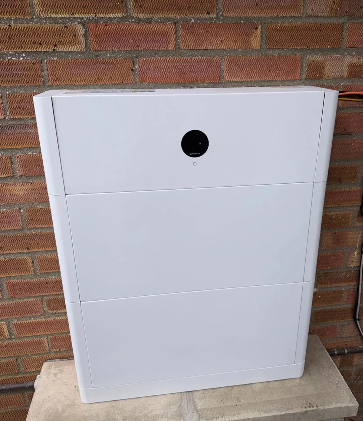 A modern battery storage unit installed against a brick wall, part of ICE Electrical Solutions's solar solutions in Diss.