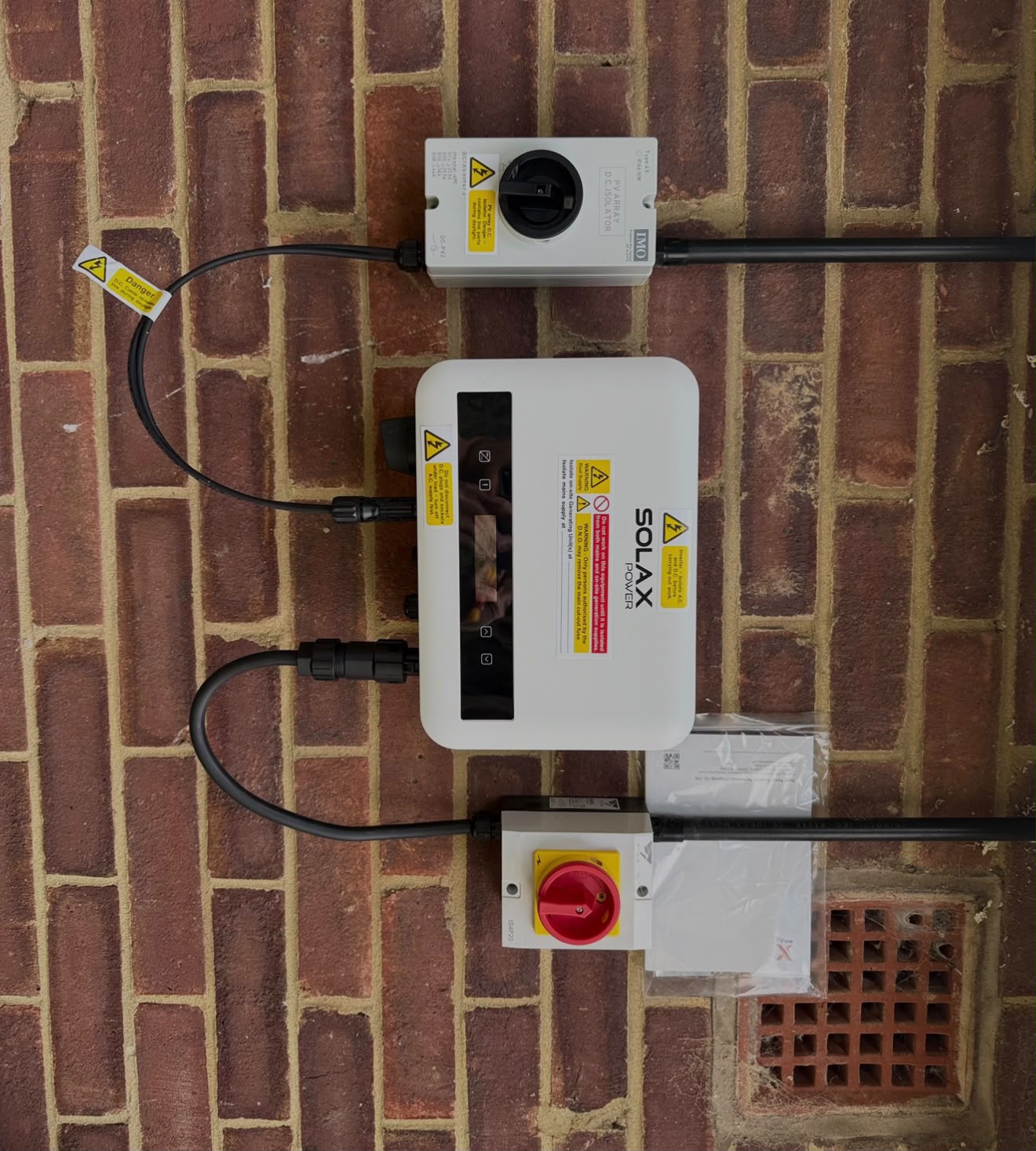 Solar panel inverter and isolator switches mounted on a brick wall, installed by {{company_name}} in {{place}}.