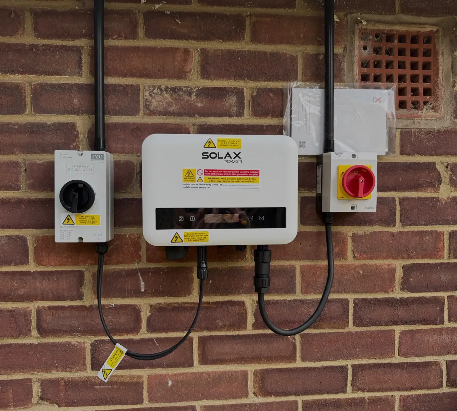 Solar panel inverter and isolator switches mounted on a brick wall, installed by ICE Electrical Solutions in Cambridge.