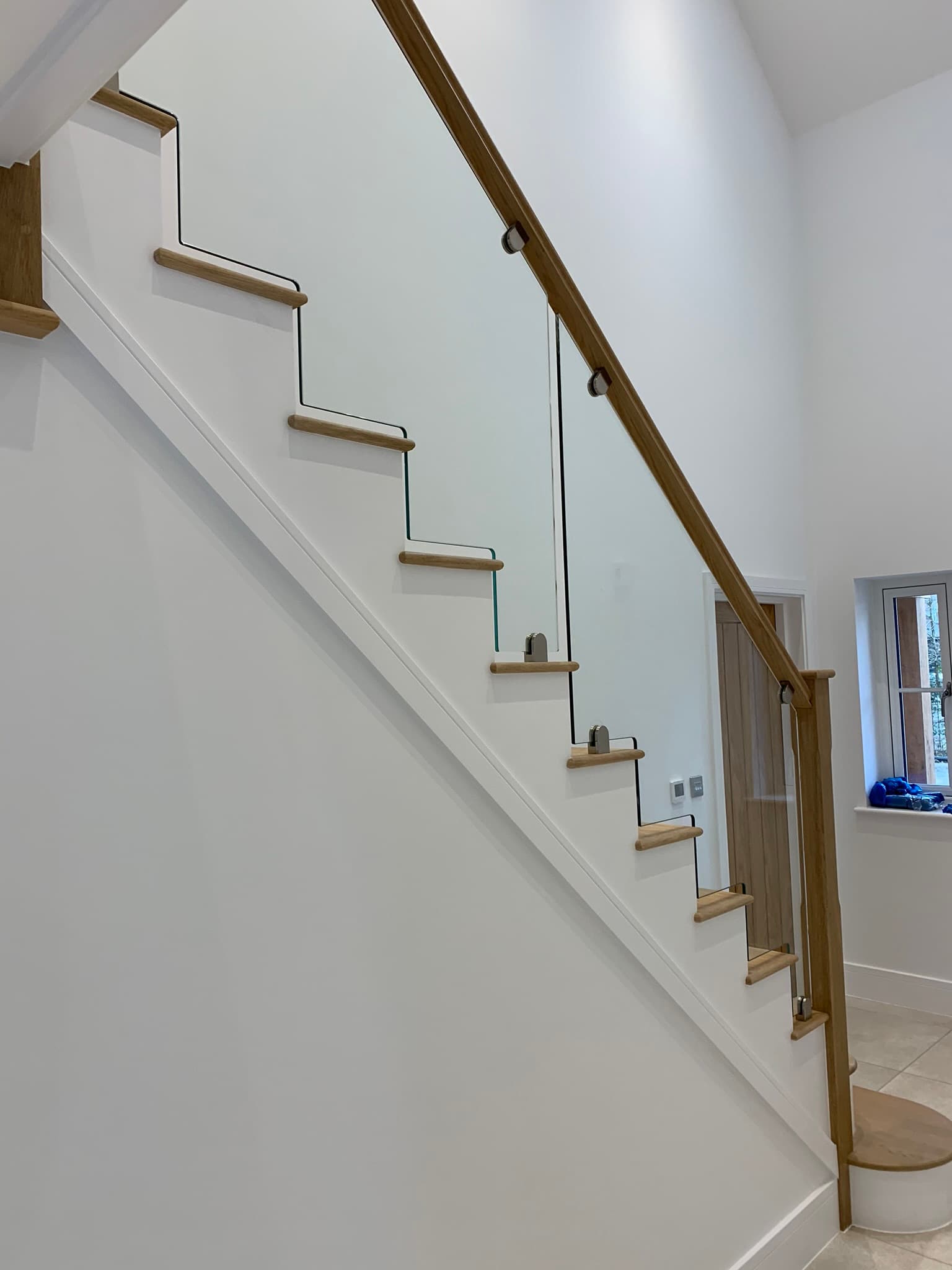 Glass balustrade with wooden handrail on a staircase, showcasing FOL Design Ltd's bespoke Glass Balustrades &amp; Handrails solutions in Duxford.
