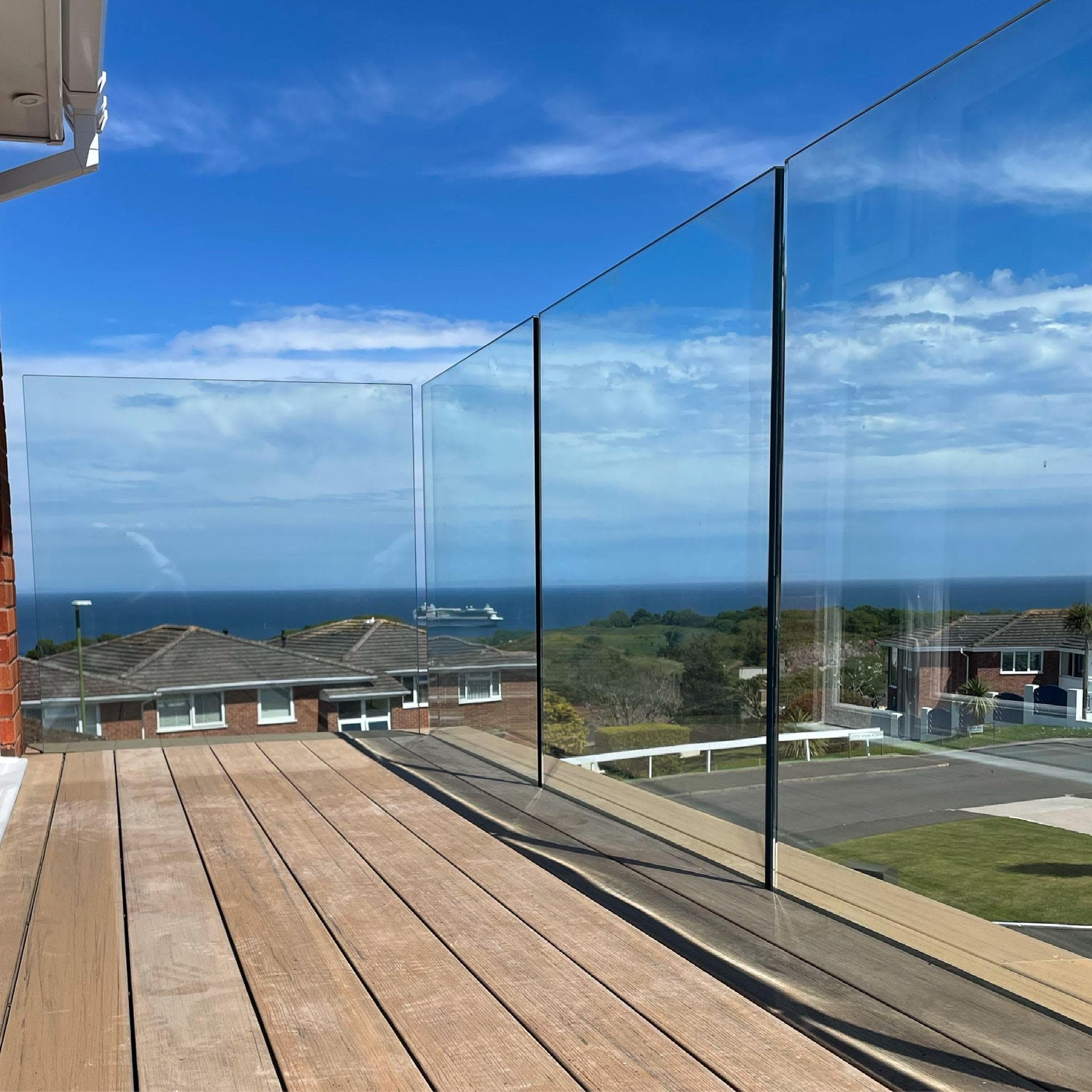 Frameless glass balustrade on a wooden deck overlooking a coastal view, offered by FOL Design Ltd in Duxford.