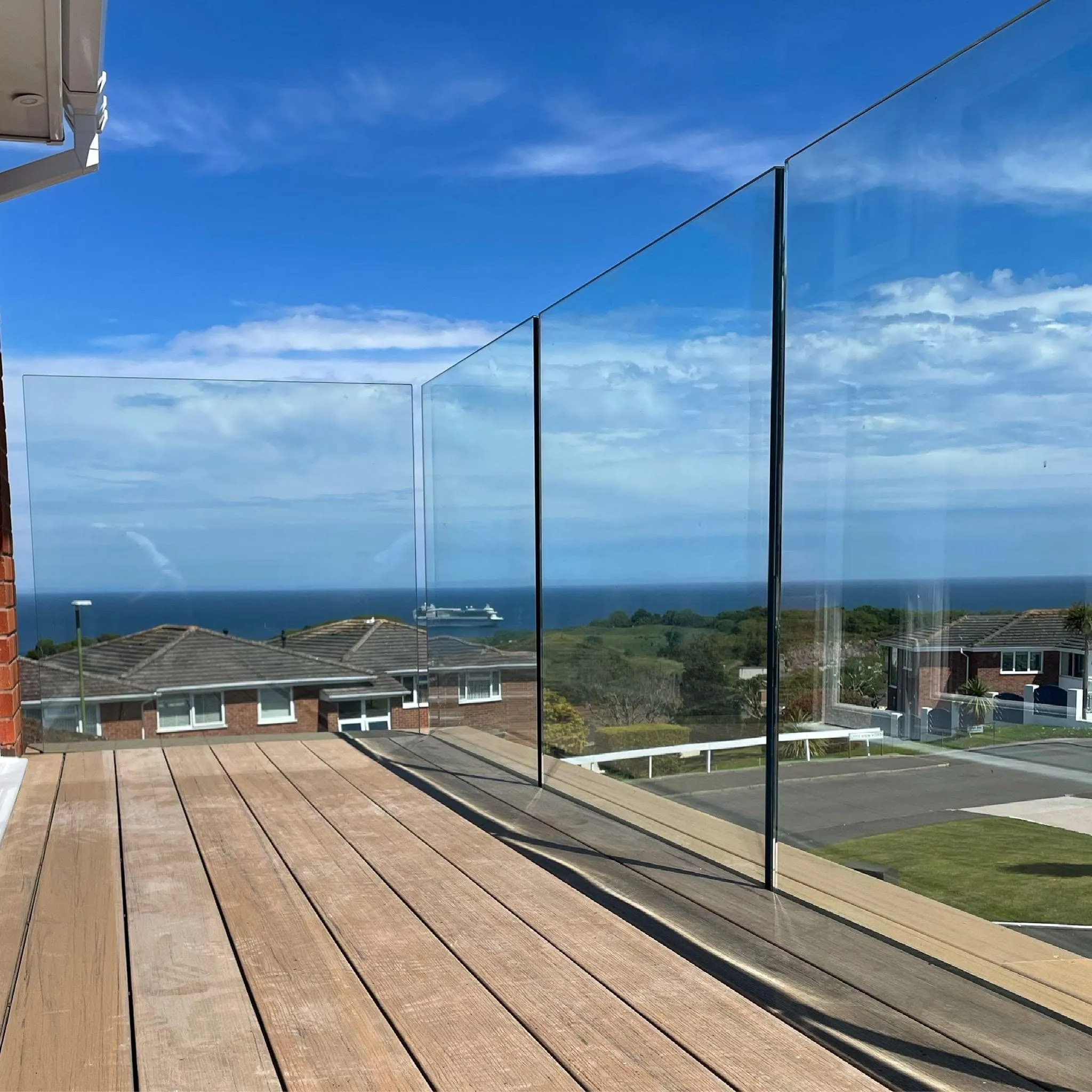 Frameless glass balustrade on a wooden deck overlooking a coastal view, offered by FOL Design Ltd in Cambridge.