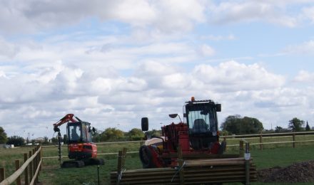Two excavators working on a grassy field under a cloudy sky, illustrating {{company_name}}'s {{search_term}} services in {{place}}.