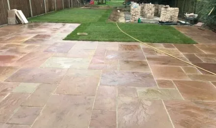 Freshly laid patio with stone slabs and adjacent lawn area, showcasing groundwork services by MJ Digger &amp; Driver Hire Services in Huntingdon.